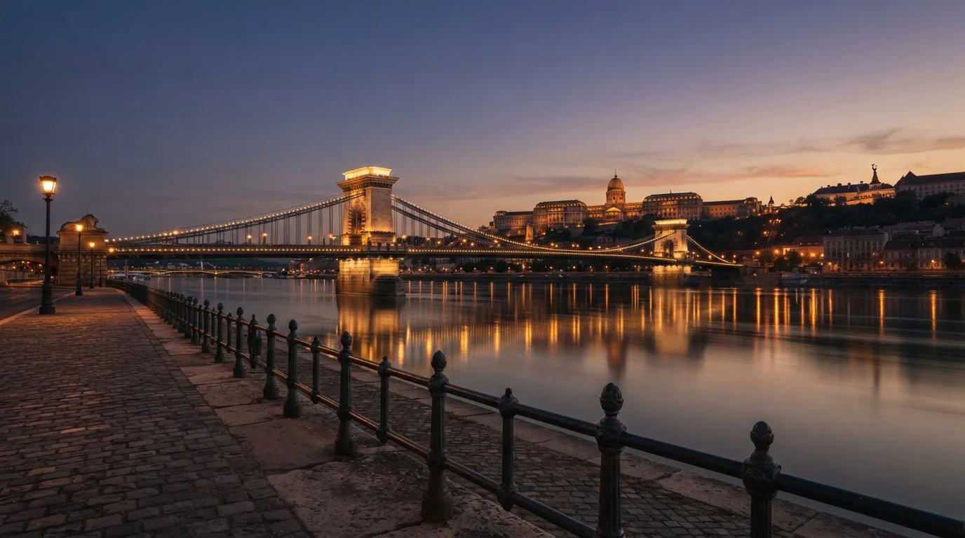 A budapesti Lánchíd esti fényekben a Duna fölött, a háttérben a budai Vár, forgalom nélküli rakpart.
